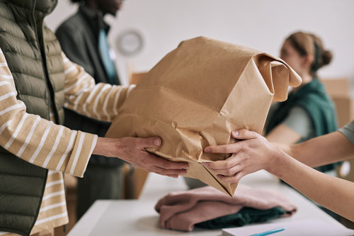 Eine Papiertüte mit Kleidung wird von Hand zu Hand weitergegeben.